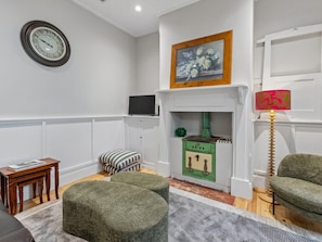 A living room with a fireplace, a clock, a television, and green upholstered furniture. - The Calton Bungalow | 3br Heritage Stay in Gawler East (Gawler East)