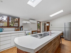 A modern kitchen with a central island, a built-in oven, and a large window providing natural light. - The Calton Bungalow | 3br Heritage Stay in Gawler East (Gawler East)