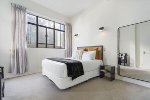A bedroom with a large bed, a bedside table, a mirror, and a window with curtains. - Corner Character 2BR at Dilworth with Balcony (Auckland Central)