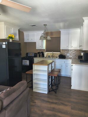 A modern kitchen with white cabinetry, a black refrigerator, a wooden island with stools, and a hanging light fixture. - Furnished 2BR/2BA Houston Home - Gated Parking (Houston)