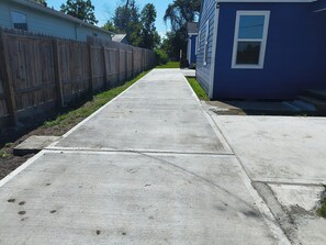 A concrete pathway leading to a residential area with a wooden fence and a blue house. - Furnished 2BR/2BA Houston Home - Gated Parking (Houston)