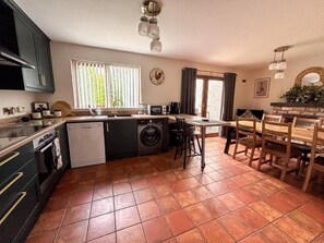 A compact kitchen with a dishwasher, washing machine, and a dining area with a table and chairs. - Bright 4BR Cottage | Enclosed Garden & Parking (Ballycastle)
