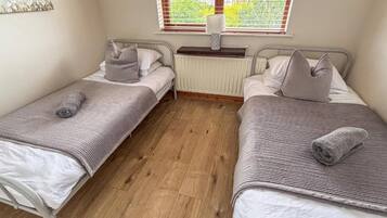 A small room with two single beds, a radiator, and a window with blinds.