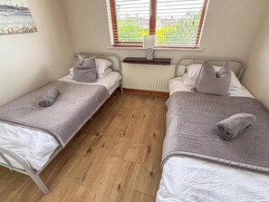 A small room with two single beds, a radiator, and a window with blinds. - Bright 4BR Cottage | Enclosed Garden & Parking (Ballycastle)
