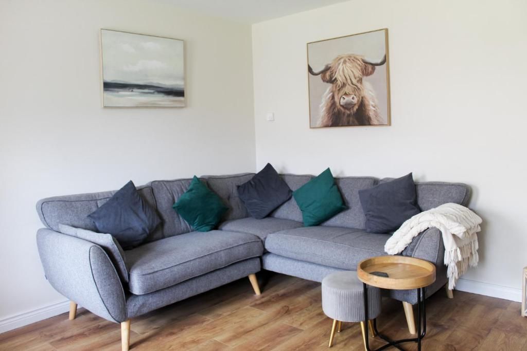 A grey sectional sofa with multiple cushions, a round wooden side table, and a framed picture of a bull on the wall.