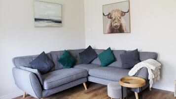 A grey sectional sofa with multiple cushions, a round wooden side table, and a framed picture of a bull on the wall.