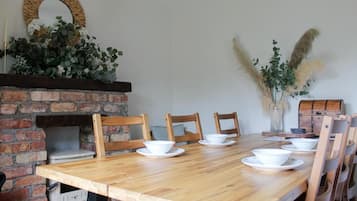 Ein Essbereich mit Kamin aus Ziegelsteinen, Holzstühlen und einem langen Holztisch, gedeckt mit weißen Schüsseln und Tellern.