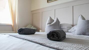 A neatly made bed with rolled towels and pillows, a window with curtains, and a framed picture on the wall.