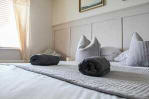 Una cama bien hecha con toallas enrolladas y almohadas, una ventana con cortinas y un cuadro en la pared.