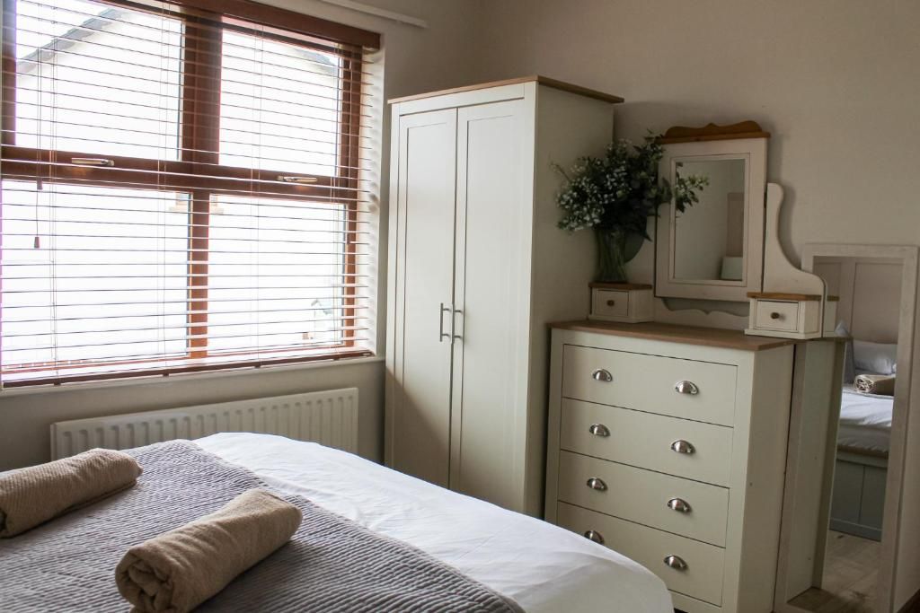 A bedroom with a bed, a dresser, a mirror, and a window with blinds.