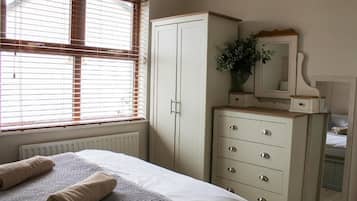 A bedroom with a bed, a dresser, a mirror, and a window with blinds.