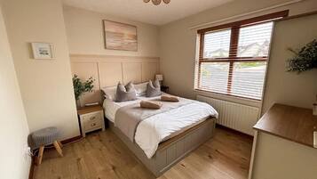 A bedroom with a bed, bedside tables, a nightstand, a window with blinds, and a hanging light fixture.