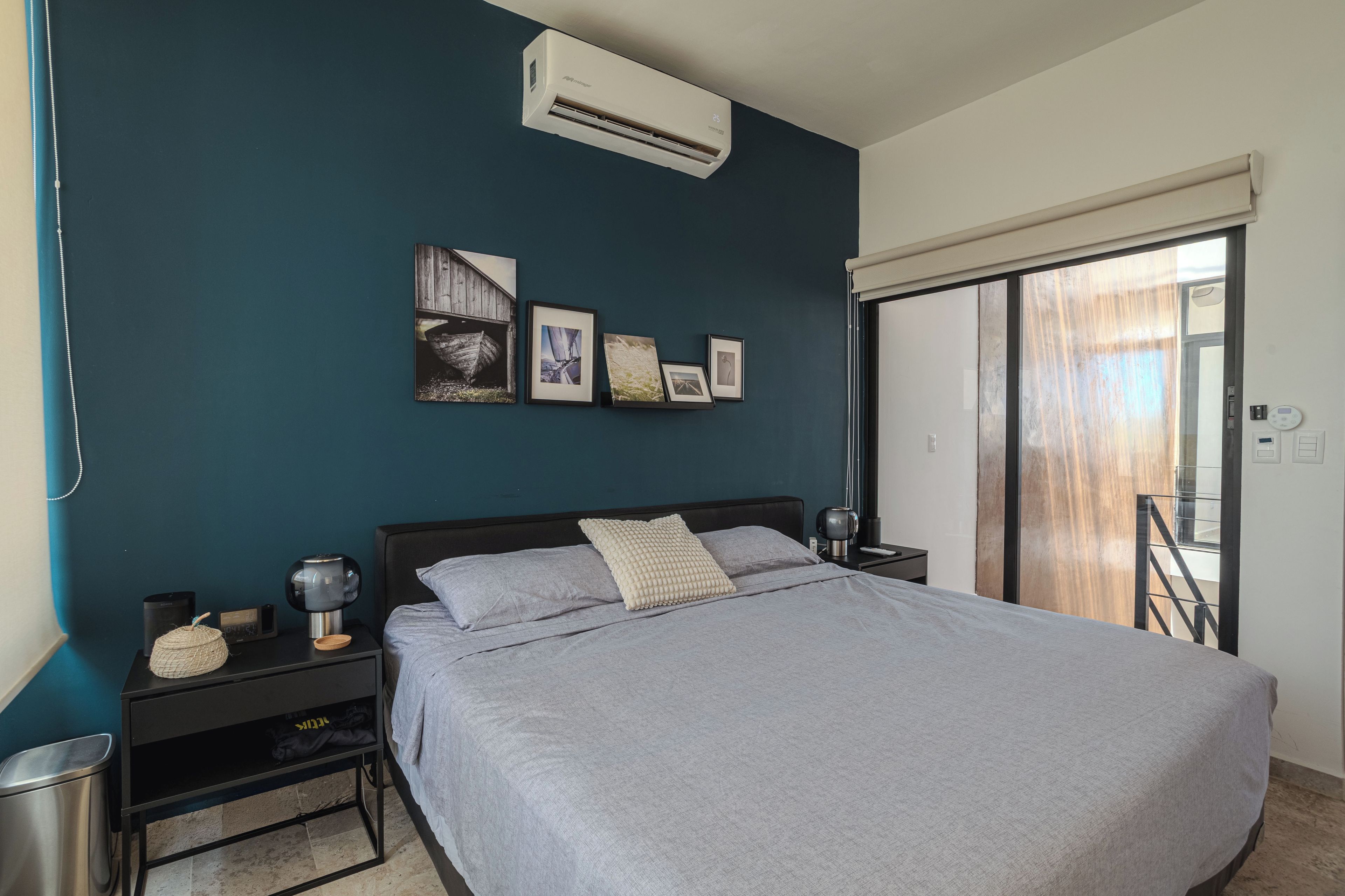 Un dormitorio con cama, mesitas de noche, aire acondicionado instalado en la pared y cuadros enmarcados.