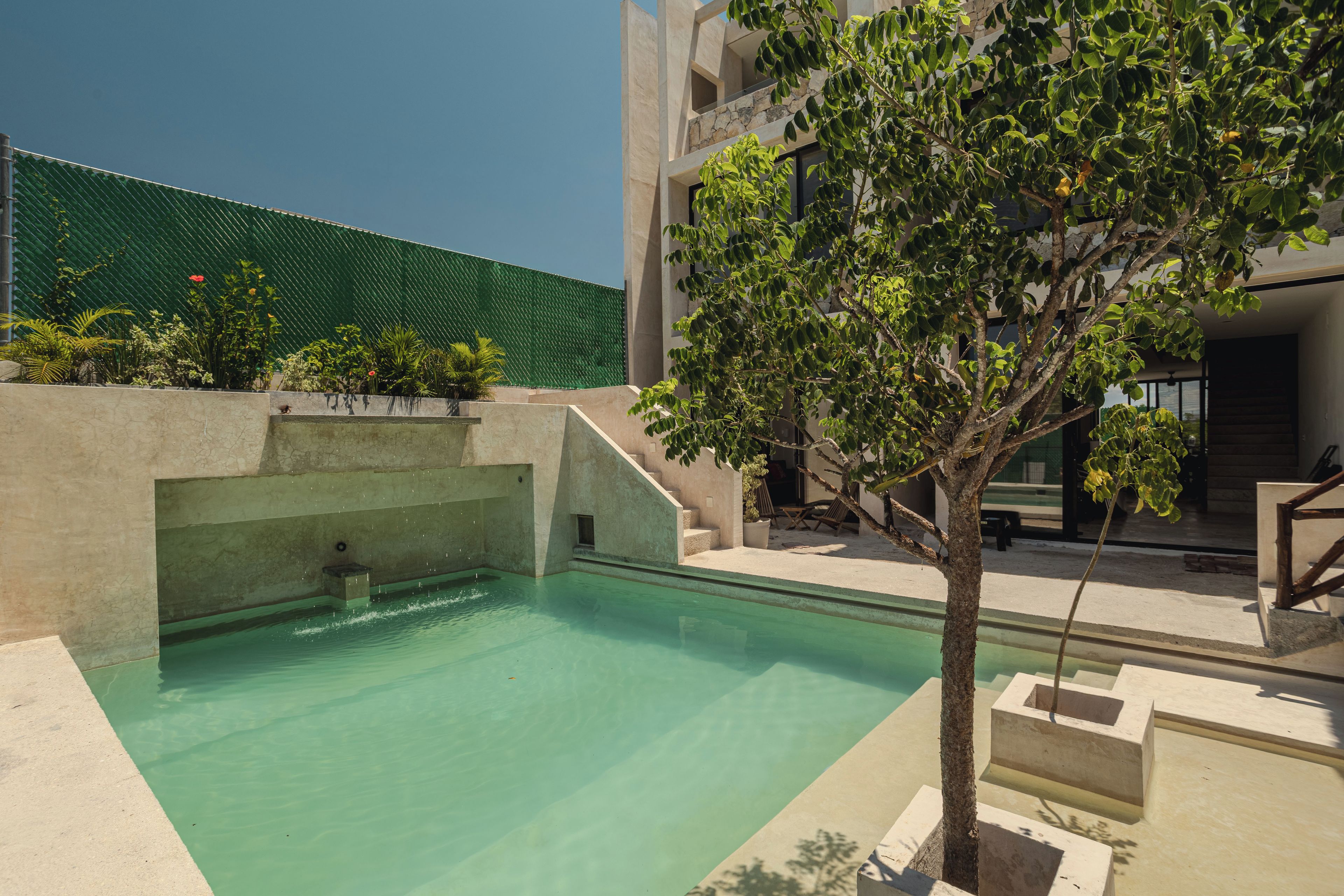 Une piscine bordée d’un mur en pierre, un arbre et un bâtiment à la façade en pierre.