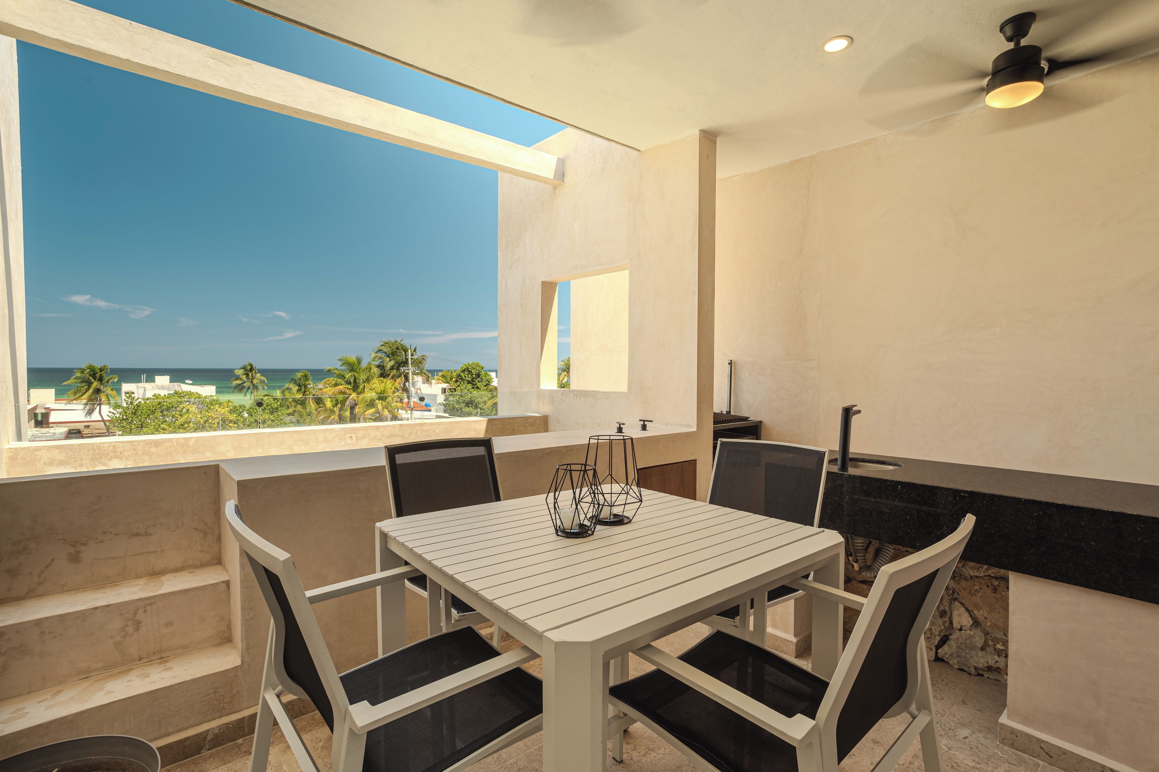 A balcony with a table and chairs, a view of the ocean, and a ceiling fan.