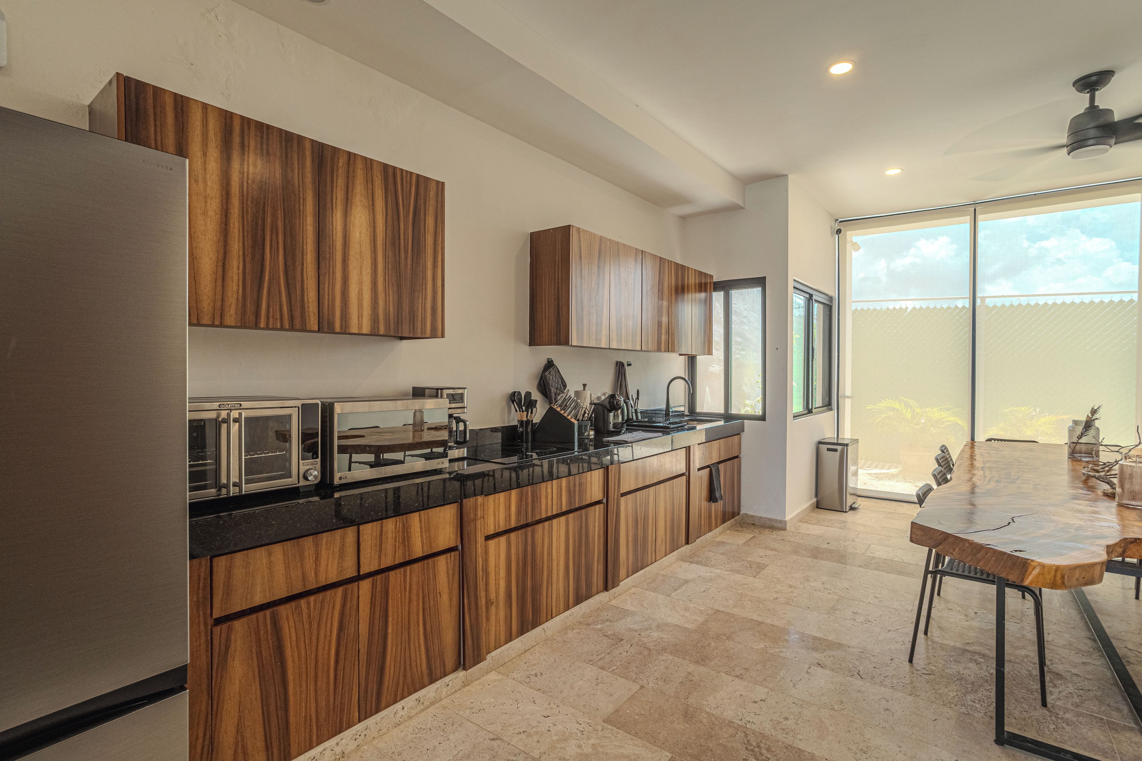 A modern kitchen with wooden cabinets, a black countertop, and a dining area with a wooden table.