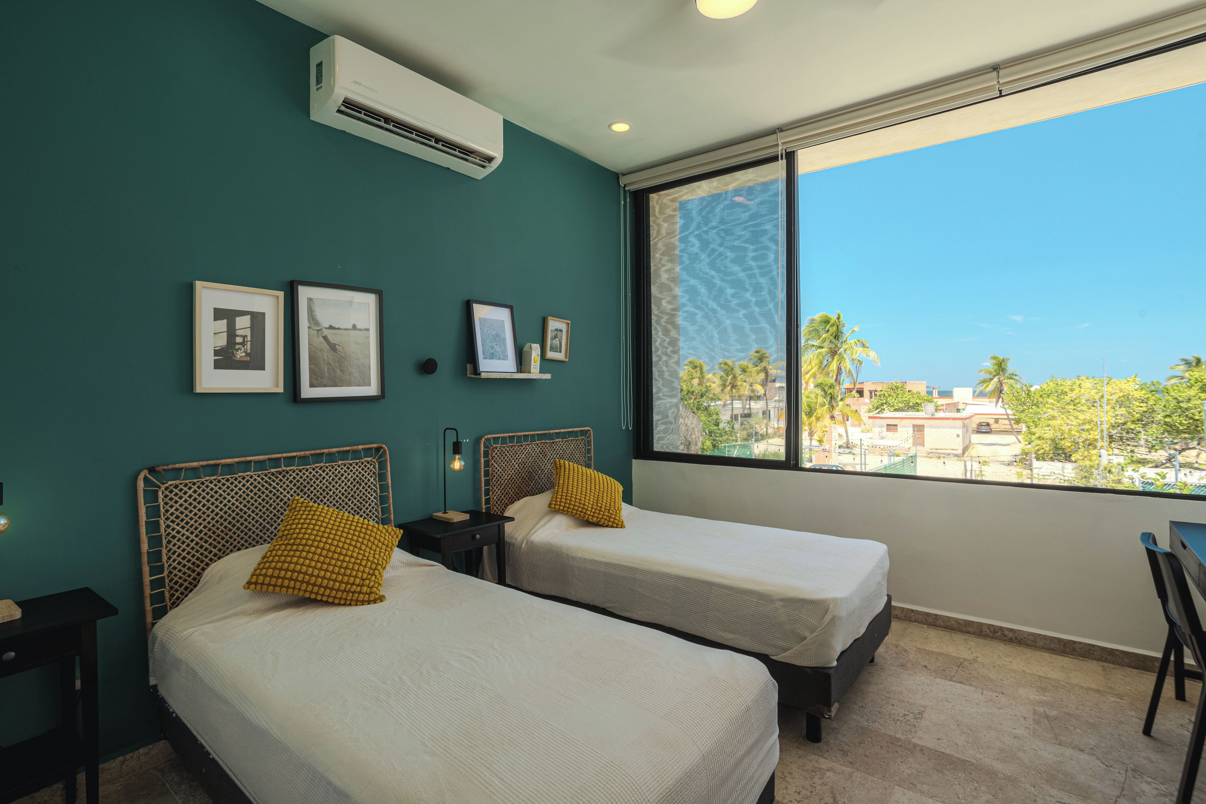 A hotel room with two beds, a large window, and wall-mounted air conditioning.