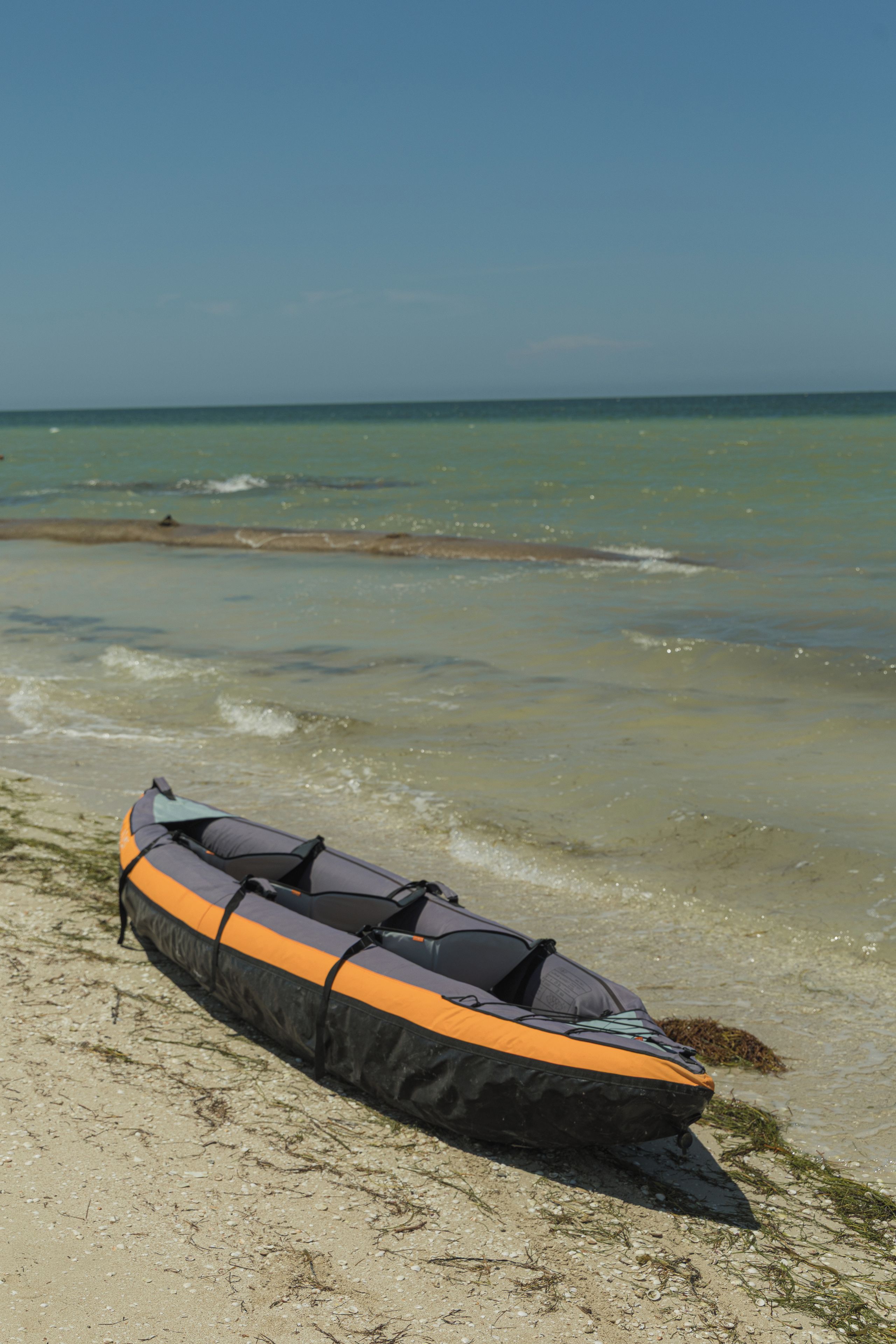 Un kayak sobre arena en una playa, con el océano al fondo.