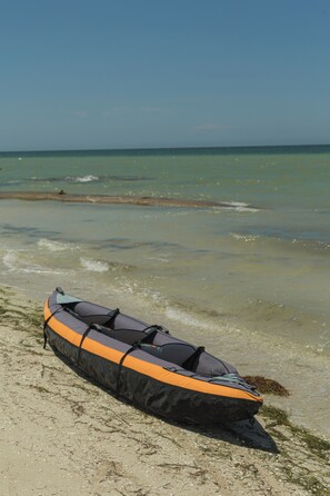 Un kayak sobre arena en una playa, con el océano al fondo.