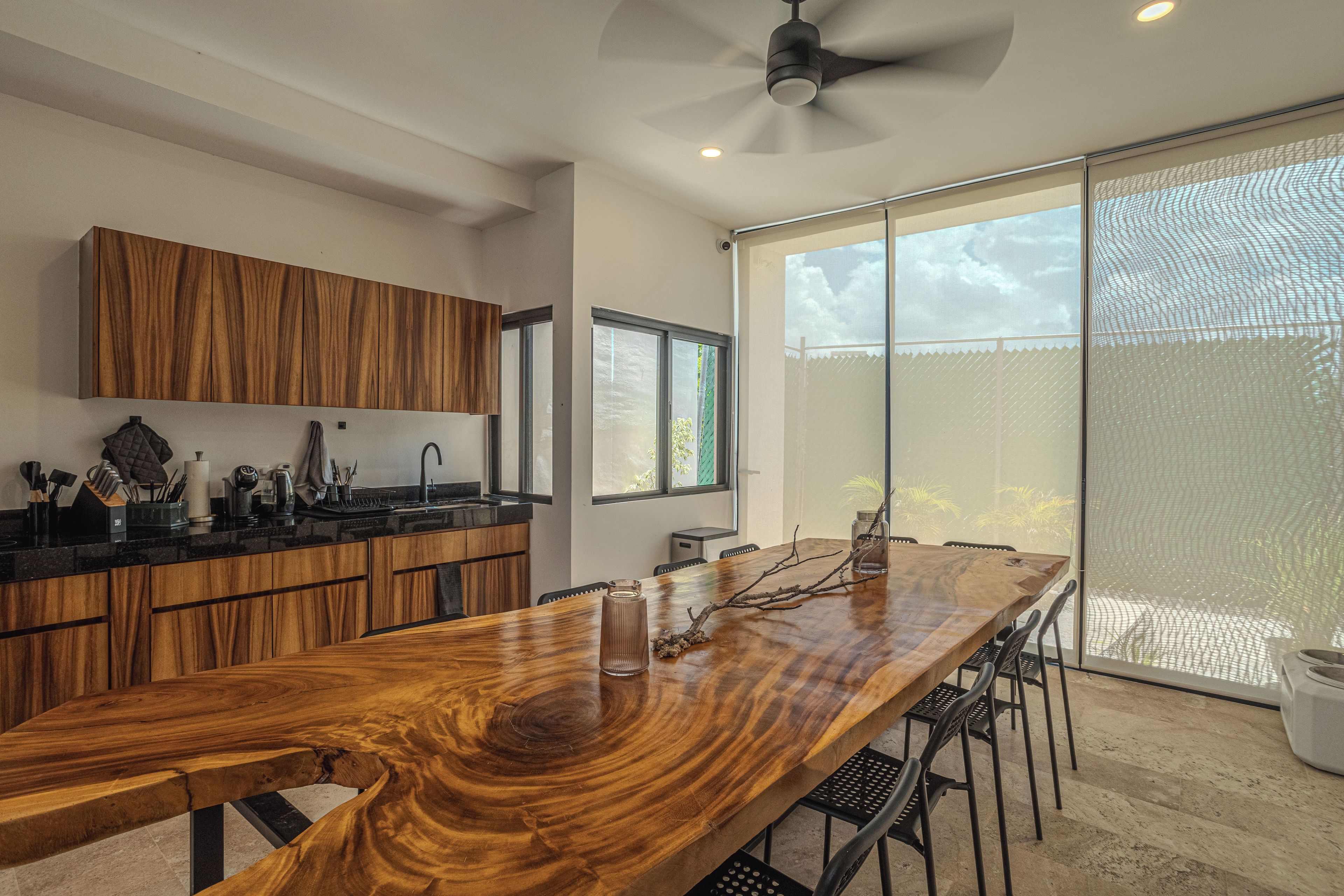 A modern kitchen with wooden cabinetry, a long dining table, and a large sliding glass door leading to a balcony.