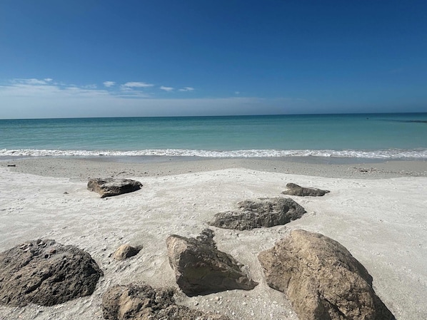 A beach with large rocks in the foreground and calm sea under a clear sky.