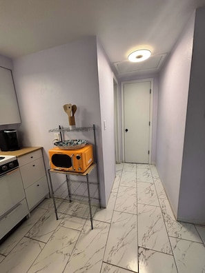 A narrow hallway with a microwave on a shelf, a stove, and a door at the end.