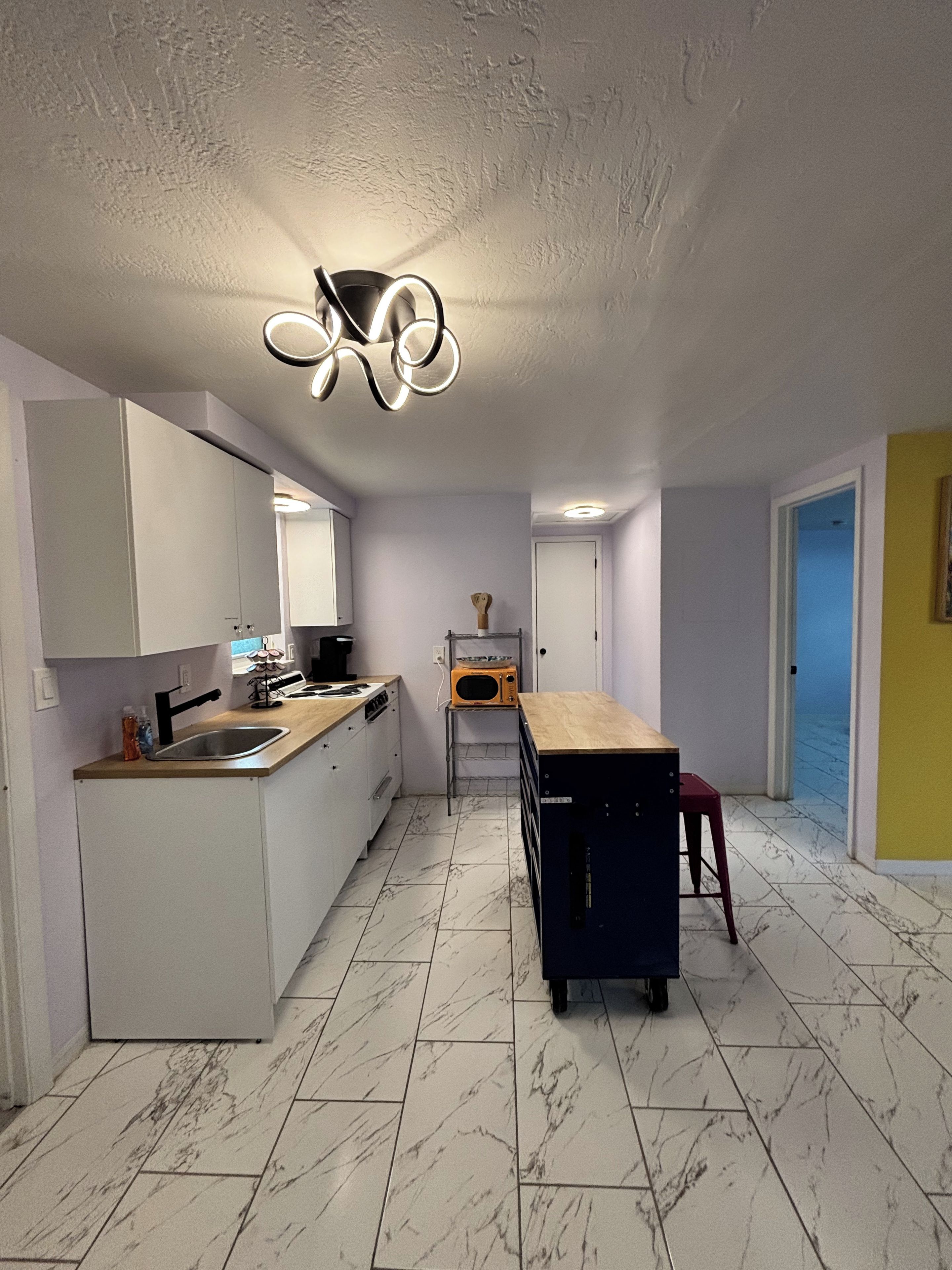 A modern kitchen with a central island, white cabinetry, and a marble floor.