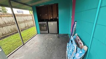 Un espace extérieur abrité, doté d’une cuisine et d’un petit jardin visible à travers la porte ouverte.