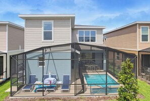 A residential property with a covered outdoor swimming pool, lounge chairs, and a clear view of the backyard. - 100" TV - Pool, Spa & Epic Game Room Villa for 14! (Kissimmee)