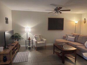 A living room with a sofa, armchair, coffee table, TV, and a ceiling fan. - Top-Floor Scottsdale Retreat - Pool, Spa & Near Old Town (Scottsdale)