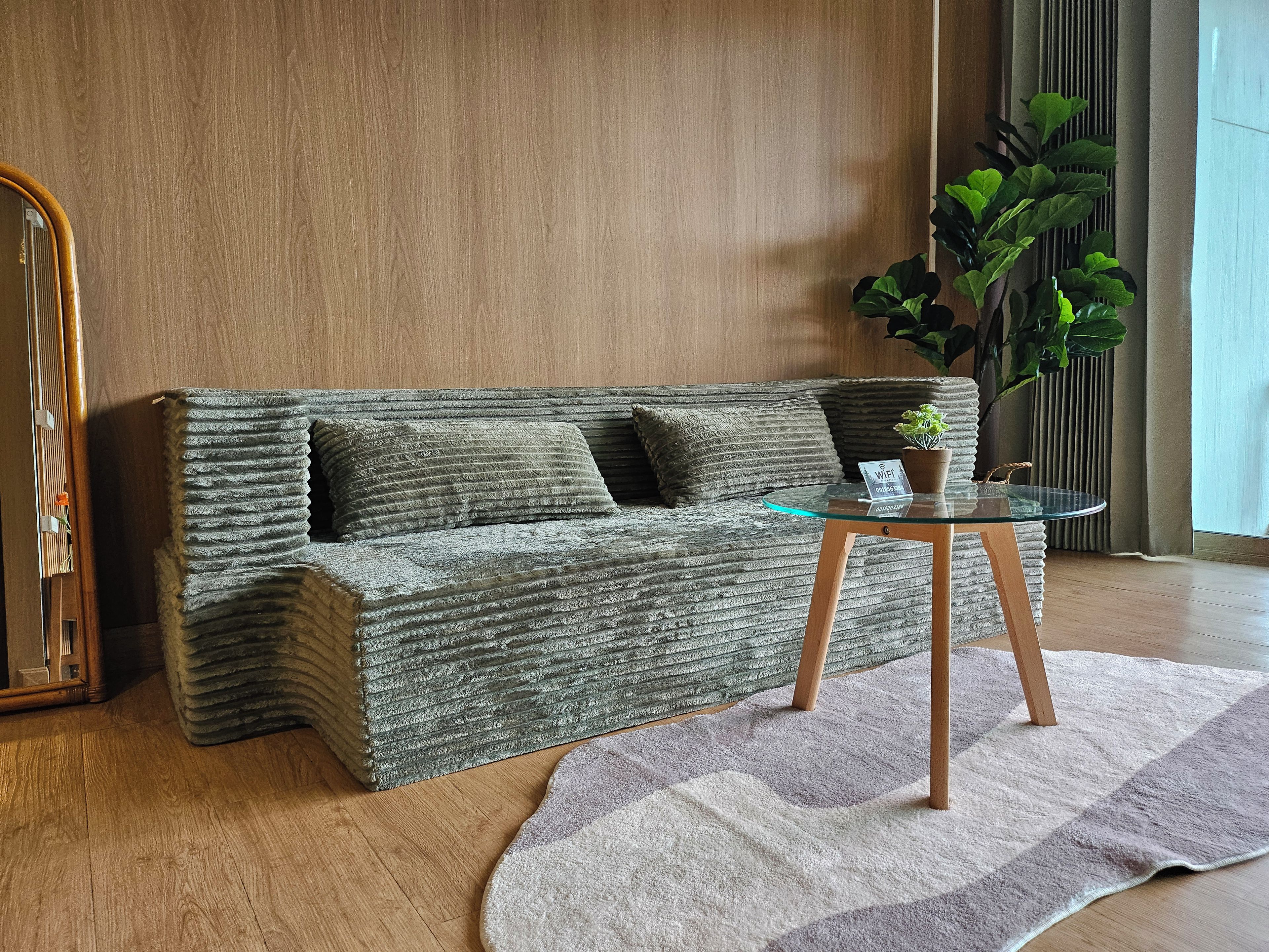 A modern living room with a textured sofa, a glass coffee table, a potted plant, and a wooden floor.