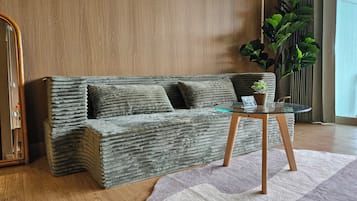 A modern living room with a textured sofa, a glass coffee table, a potted plant, and a wooden floor.