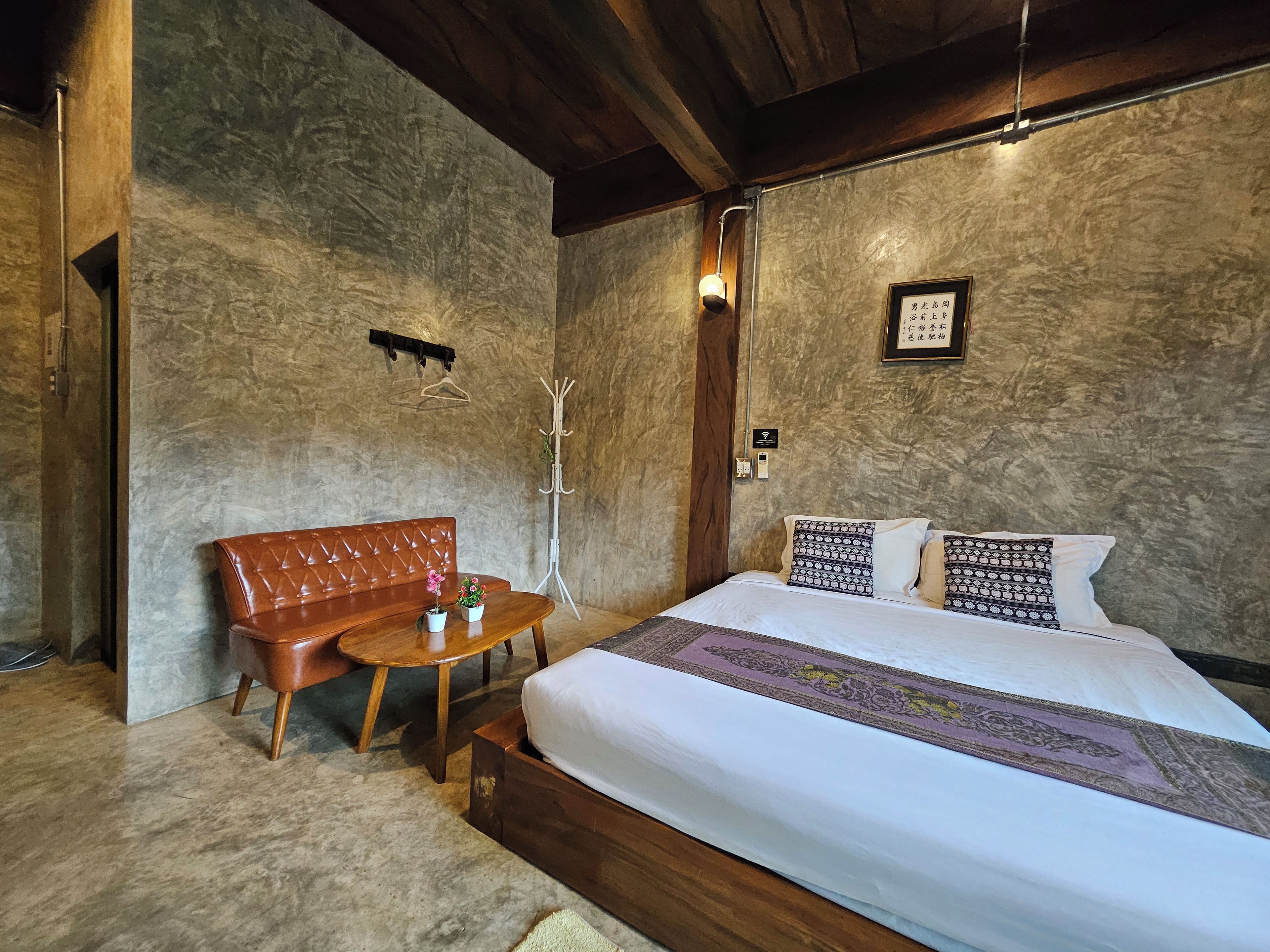A hotel room with a bed, a wooden bench, a small table, and a coat rack.