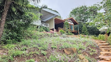 Una casa moderna con terraza de madera, rodeada de abundante vegetación y plantas en flor.