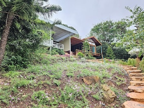 Una casa moderna con terraza de madera, rodeada de abundante vegetación y plantas en flor.