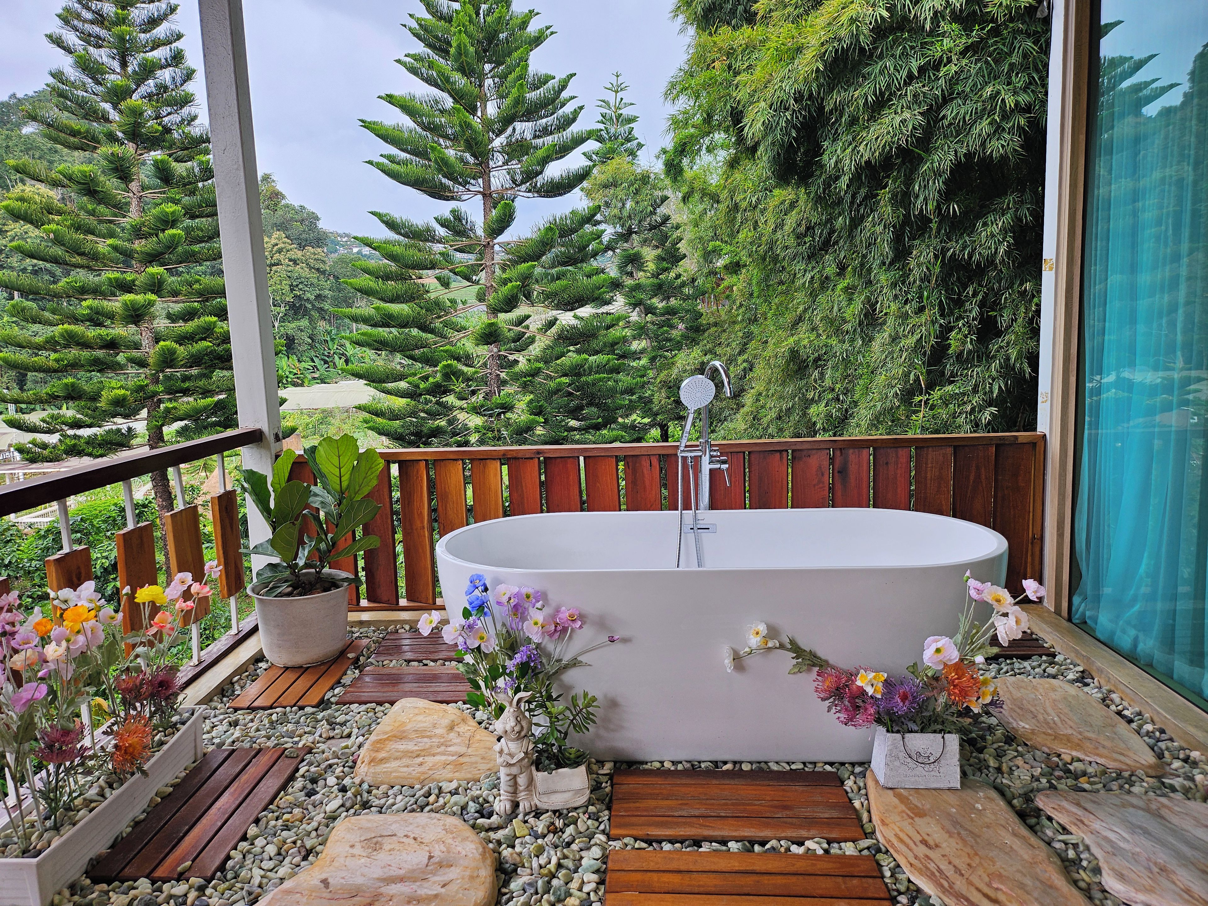 Ein Wellnessbereich mit freistehender Badewanne, umgeben von einer Holzdielen-Terrasse, Topfpflanzen und einem Kiesweg.