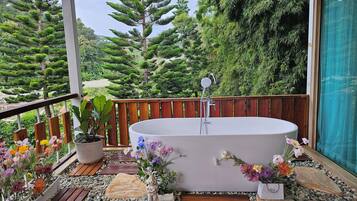 Ein Wellnessbereich mit freistehender Badewanne, umgeben von einer Holzdielen-Terrasse, Topfpflanzen und einem Kiesweg.