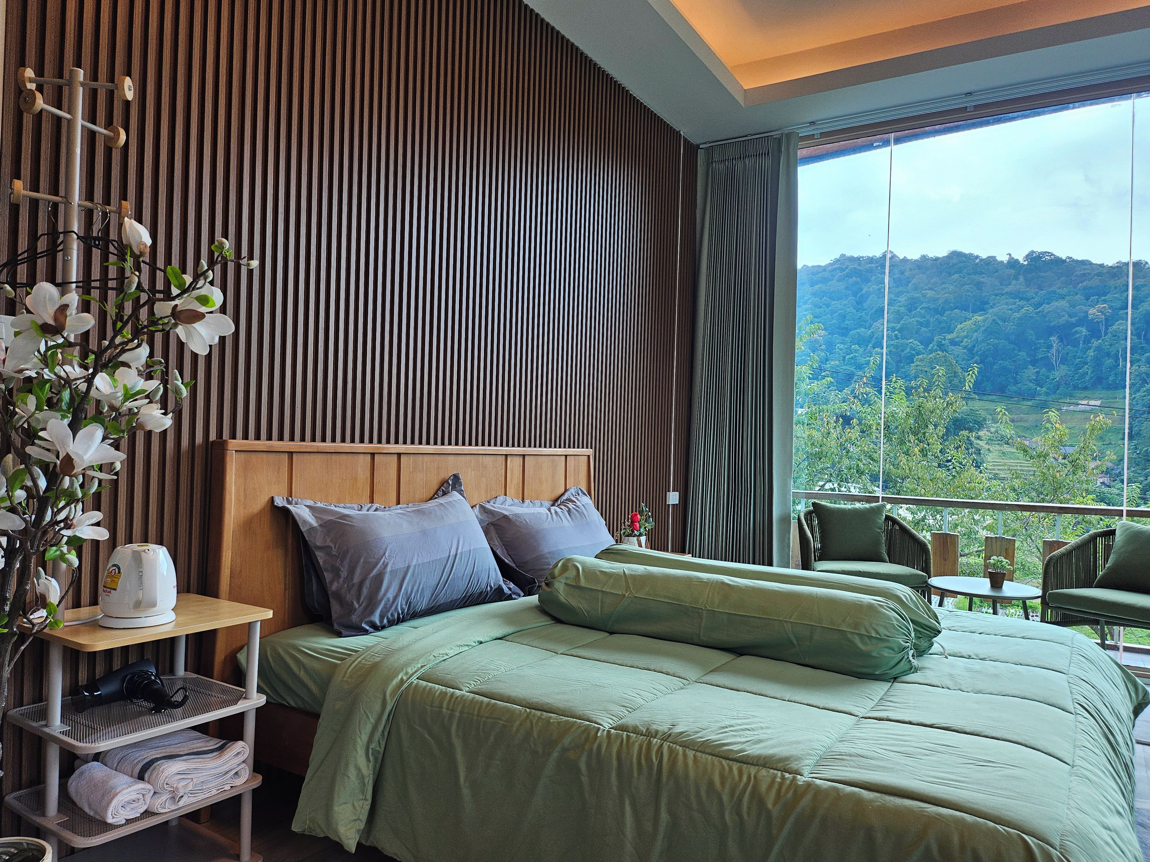 A hotel room with a bed, a nightstand, a window with a view of the landscape, and a chair by the window.