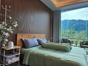 Habitación de hotel con una cama, una mesita de noche, una ventana con vistas al paisaje y una silla junto a la ventana.