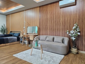 Una sala moderna con sofá, una mesa de centro de cristal, un escritorio con silla, cama y una planta en maceta.