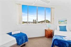 A hotel room with two beds, a window with a view of the landscape, a small wooden nightstand, and a painting on the wall. - Miami Beachside Oceanfront Apartment (Gold Coast)