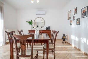 A dining area with a wooden table and chairs, a round mirror, and a wall-mounted air conditioner. - Villa Mulberry Tree in Rethymno (Rethymno)