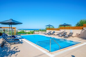 A pool area with lounge chairs and umbrellas, a view of the sea, and a clear sky. - Villa Mulberry Tree in Rethymno (Rethymno)