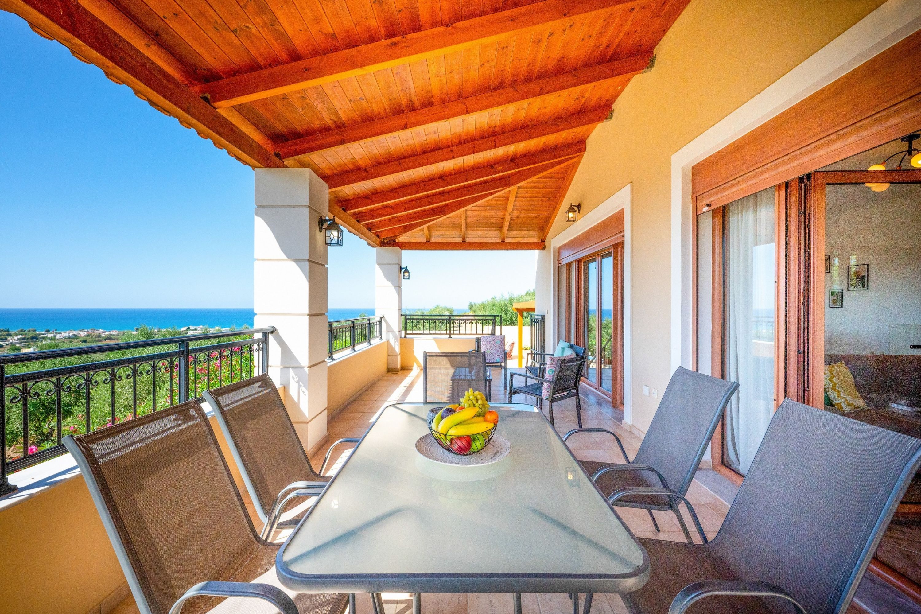 A covered outdoor seating area with a table and chairs, a view of the sea, and a balcony with a railing.