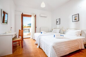 A hotel room with two beds, a desk, a chair, and a balcony with a view. - Villa Mulberry Tree in Rethymno (Rethymno)
