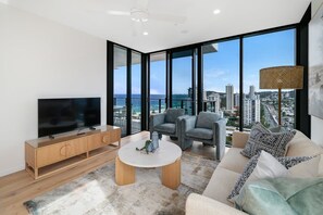 Ein modernes Wohnzimmer mit Flachbildfernseher, Couchtisch und einer Sitzecke mit Blick auf Stadt und Meer.