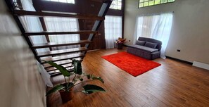 Un salon moderne avec un escalier en bois, un canapé gris, un tapis rouge et une plante en pot.