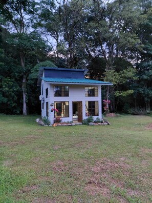 Ein zweistöckiges Haus mit blauem Dach, umgeben von einem grünen Rasen und Bäumen.