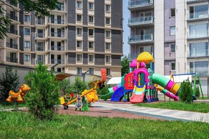 A playground with various play structures, including slides and swings, surrounded by a residential area with multi-story buildings. - Zarafshan 49 (Tashkent)