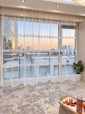 A room with a large window covered by sheer curtains, a potted plant, and a small table with a can and gummy bears. - Zarafshan 49 (Tashkent)